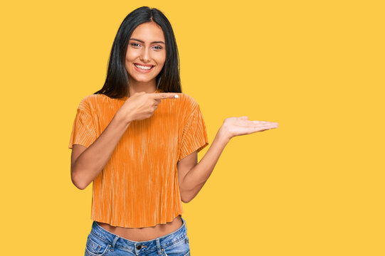 Young brunette arab woman wearing casual clothes amazed and smiling to the camera while presenting with hand and pointing with finger.