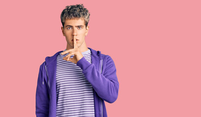 Young handsome man wearing casual purple sweatshirt asking to be quiet with finger on lips. silence and secret concept.