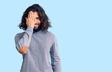 Young arab man wearing casual clothes covering one eye with hand, confident smile on face and surprise emotion.