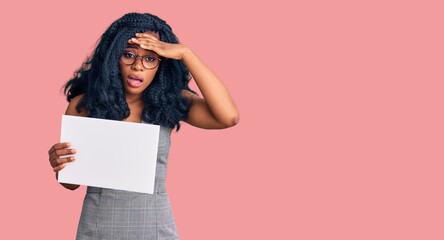 Beautiful african american woman holding blank empty banner stressed and frustrated with hand on head, surprised and angry face