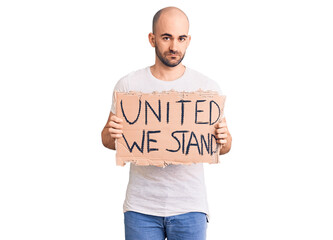 Young handsome man holding united we stand banner thinking attitude and sober expression looking self confident