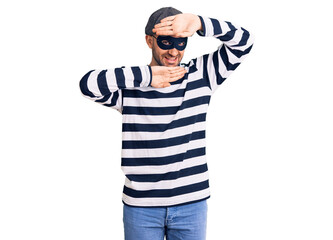 Young handsome man wearing burglar mask smiling cheerful playing peek a boo with hands showing face. surprised and exited