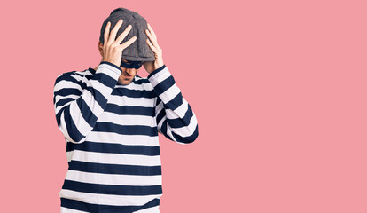 Young handsome man wearing burglar mask suffering from headache desperate and stressed because pain and migraine. hands on head.