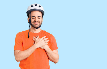 Young handsome man wearing bike helmet smiling with hands on chest with closed eyes and grateful gesture on face. health concept.