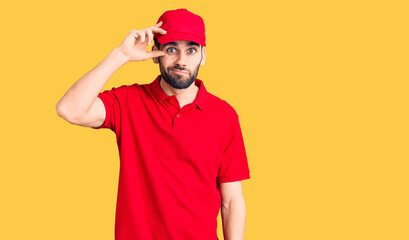 Young handsome man with beard wearing delivery uniform worried and stressed about a problem with hand on forehead, nervous and anxious for crisis