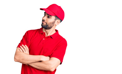 Young handsome man with beard wearing delivery uniform looking to the side with arms crossed convinced and confident