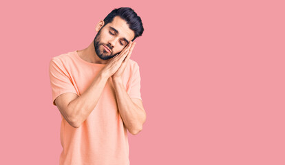 Young handsome man with beard wearing casual t-shirt sleeping tired dreaming and posing with hands together while smiling with closed eyes.