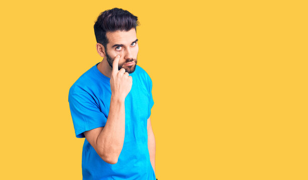Young handsome man with beard wearing casual t-shirt pointing to the eye watching you gesture, suspicious expression