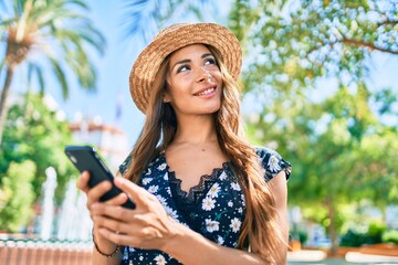 Young hispanic woman on vacation using smartphone at street of city.