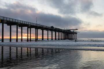 Scripps Pier in San Diego California during sunset with moody clouds over waves and sand.