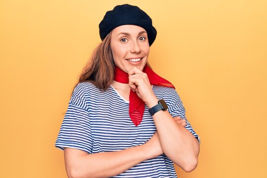 Young beautiful blonde woman wearing french fashion style with scarf and beret smiling looking confident at the camera with crossed arms and hand on chin. thinking positive.