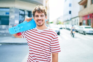 Young caucasian skater man smiling happy holding skate walking at street of city. © Krakenimages.com