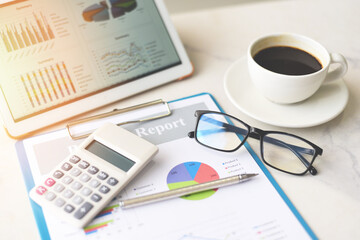 Fototapeta premium Business graphs chart on a tablet computer technology on the table with coffee cup on desk and calculator - Sale report money analyzing