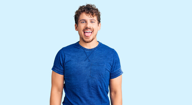 Young handsome man with curly hair wearing casual clothes sticking tongue out happy with funny expression. emotion concept.