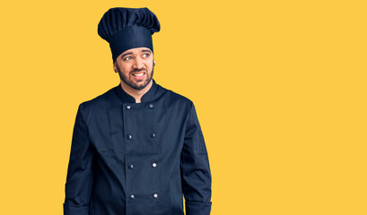 Young hispanic man wearing cooker uniform looking away to side with smile on face, natural expression. laughing confident.
