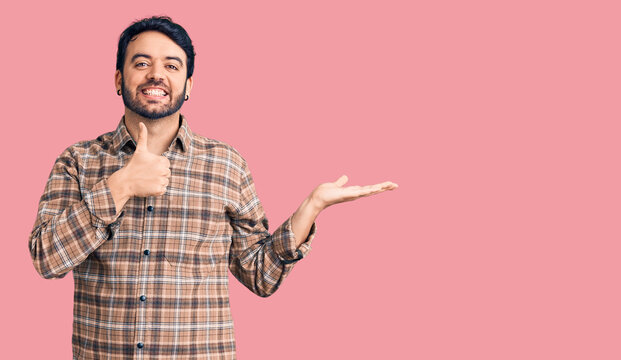 Young hispanic man wearing casual clothes showing palm hand and doing ok gesture with thumbs up, smiling happy and cheerful