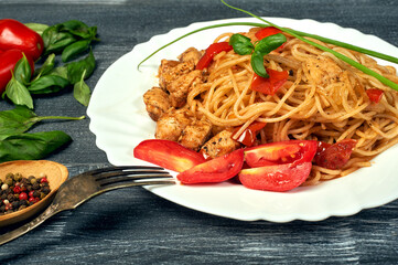 Classic Italian pasta with spaghetti in tomato sauce and chicken on a plate on a dark background . The view from the top .
