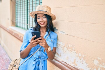 Young indian woman leaning on the wall using smartphone at the city