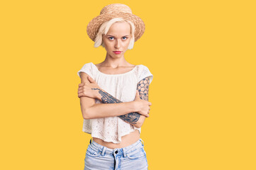 Young blonde woman with tattoo wearing summer hat skeptic and nervous, disapproving expression on...