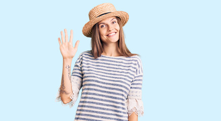 Obraz na płótnie Canvas Beautiful caucasian woman wearing summer hat showing and pointing up with fingers number five while smiling confident and happy.