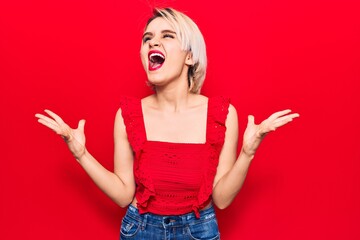 Young beautiful blonde woman wearing casual clothes crazy and mad shouting and yelling with aggressive expression and arms raised. frustration concept.