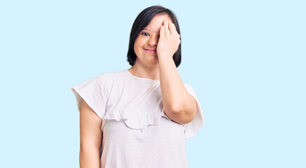 Brunette woman with down syndrome wearing casual white tshirt covering one eye with hand, confident smile on face and surprise emotion.
