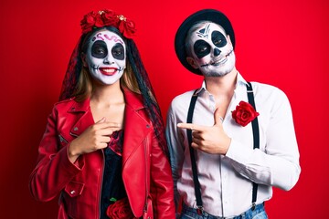 Couple wearing day of the dead costume over red cheerful with a smile on face pointing with hand and finger up to the side with happy and natural expression
