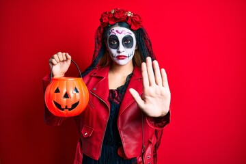 Woman wearing day of the dead costume holding pumpkin with open hand doing stop sign with serious and confident expression, defense gesture