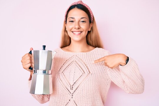 Young brunette woman holding italian coffee maker pointing finger to one self smiling happy and proud