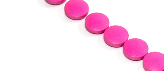 Close-up of pink round tablets arranged diagonally in a row on a white background, banner