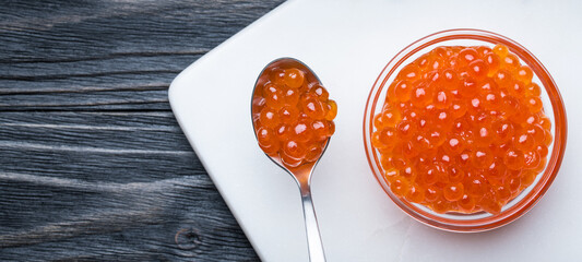 Red Caviar on a spoon and glass bowl. Salmon fish caviar. Raw seafood. Luxury delicacy food. Dark natural wooden background.