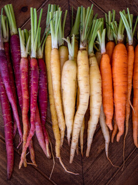 Rainbow carrots with trimmed tops arranged by color on wooden tray in vertical