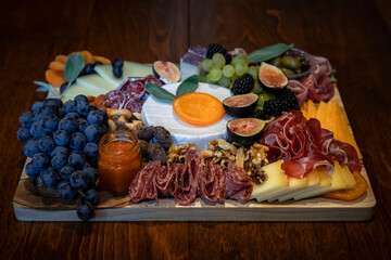 Food board with cured meats prosciutto, salami and coppa, hard and soft cheeses brie, cheddar,...
