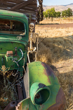 Skeleton Leaning Against An Old Green Truck In A Dead Grass Field