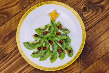 Christmas tree made of kiwi slices and pomegranate on wooden table. Top view. Creative idea for Christmas and New Year festive desserts. Funny food idea for kids