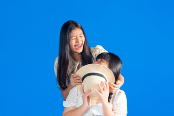Two asian Girlfriends, sisters having fun hugging and smiling on blue background.