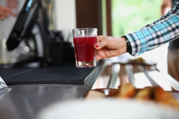 Fototapeta na wymiar Woman's hand holds glass in cafe with red liquid similar to fruit drink or jelly. Self service cafe concept