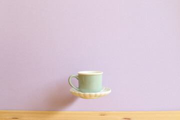 Mint green coffee cup floating on wooden table with light purple background. copy space