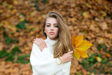 Beautiful fashion girl with long blonde hair, wearing stylish dress posing in autumn park. Outdoor portrait. Female autumn fashion concept.