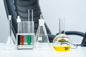 Transparent test tubes on background of empty chair. Laboratory glass on table. Concept - use of laboratory glass by chemist. Laboratory glass for sale. Equipment for lab. Labware of various shapes.