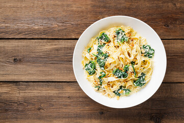 Pasta fettuccine with spinach in creamy cheese sauce on a wooden background.