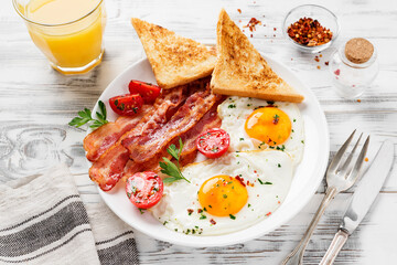 American breakfast with two fried eggs,tomato salad,bacon, toast and orange juice .