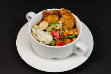 Soto Betawi. Traditional Chicken soup from Betawi, Jakarta. Served in a white bowl on black background
