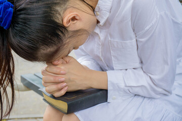 Naklejka premium Woman hands praying with a bible in her knees outdoors