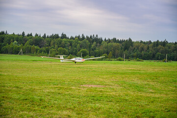 a glider is landed on a green grass of  an airdrome field in russian countryside