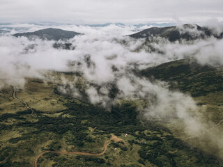 White clouds in the mountains. Clouds are above it and trees on the hill.