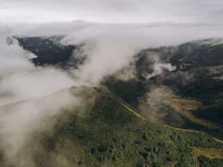 White clouds in the mountains. Clouds are above it and trees on the hill.