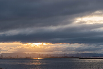 Fototapeta na wymiar 兵庫県神戸市から大阪湾の夜明け。厚い雲に覆われた空に太陽の光が現れる
