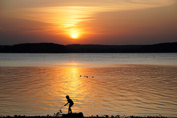 Fototapeta na wymiar Evening by the lake. Beautiful sunset and silhouette of a girl on the background of reflection.