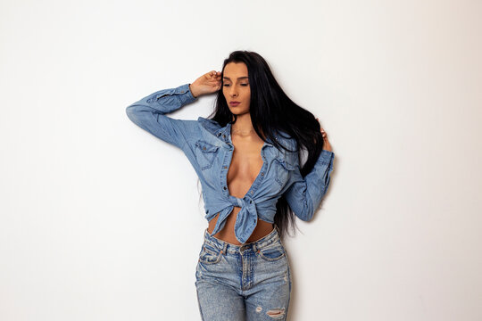 Beautiful sexy young woman in jeans stranding in front of white wall and posing